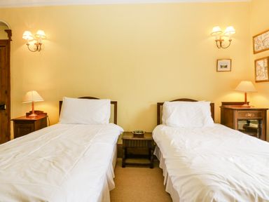 A bedroom with two single beds bedside tables lamps and wall sconces at Wheelbarrow Castle in Leominster