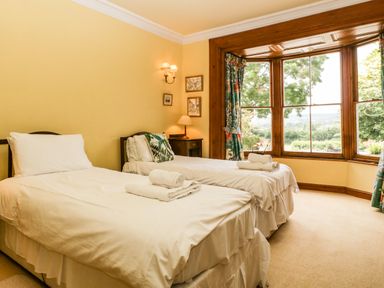 A bedroom with two single beds white bedding and towels on the beds a wooden bay window with curtains and a nightstand with a lamp at Wheelbarrow Castle in Leominster