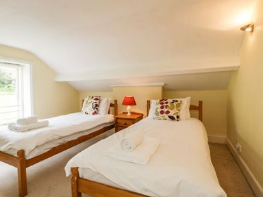 A bedroom with two single beds with white bedding and patterned pillows and a nightstand with a red lamp between them at Wheelbarrow Castle in Leominster