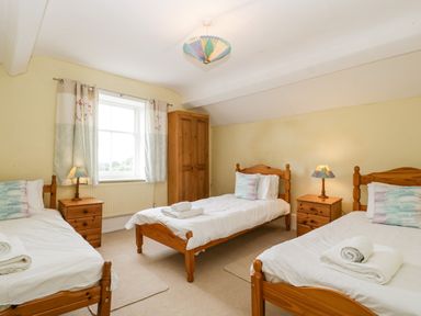 A bedroom with three single wooden beds white bedding two bedside tables with lamps a window with curtains and a wooden wardrobe at Wheelbarrow Castle in Leominster
