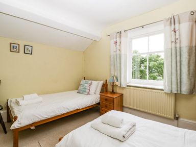 A bedroom with two single beds a wooden nightstand with a lamp and a window with curtains at Wheelbarrow Castle in Leominster