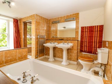 A bathroom with a bathtub double sinks a toilet and a window with red curtains at Wheelbarrow Castle in Leominster