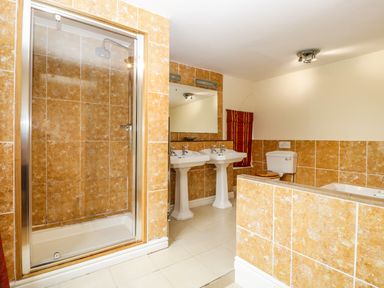 A bathroom with a shower cubicle two pedestal sinks a toilet and a bathtub with tiled walls at Wheelbarrow Castle in Leominster