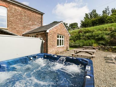 An outdoor patio area with a blue hot tub and wooden picnic tables by a stone house at Wheelbarrow Castle in Leominster