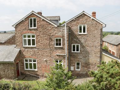 A stone house with multiple windows pipes and a red door surrounded by greenery at Wheelbarrow Castle in Leominster