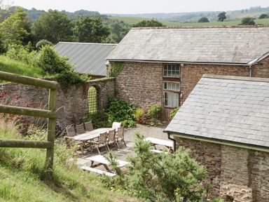 An outdoor courtyard with wooden tables and chairs next to stone buildings with slate roofs surrounded by greenery at Wheelbarrow Castle in Leominster