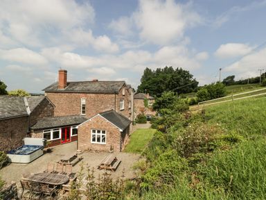 An outdoor area with wooden tables and chairs a hot tub and grassy hillside at Wheelbarrow Castle in Leominster