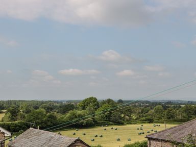 A rural field with round hay bales and trees in the background at Wheelbarrow Castle in Leominster
