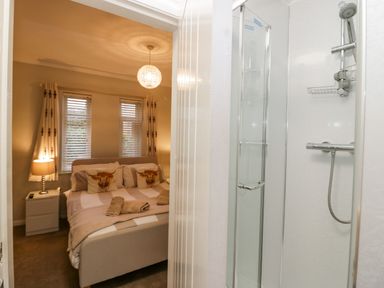 A bedroom with a double bed and bedside table with lamp visible through an open door next to a shower cubicle at Sandown in Bowness-on-Windermere