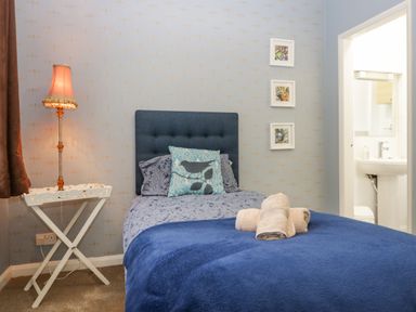 A bedroom with a single bed blue headboard and bedding towels on bed a lamp on a side table and three pictures on the wall at Sandown in Bowness-on-Windermere