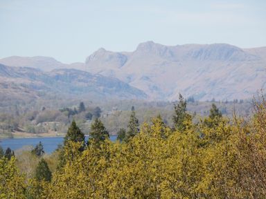 A view of a lake with trees in the foreground and hills in the background at Sandown in Bowness-on-Windermere