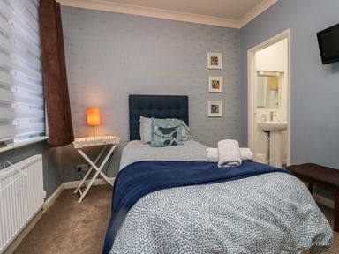 A bedroom with a single bed a bedside table with a lamp and an en suite bathroom at Sandown in Bowness-on-Windermere