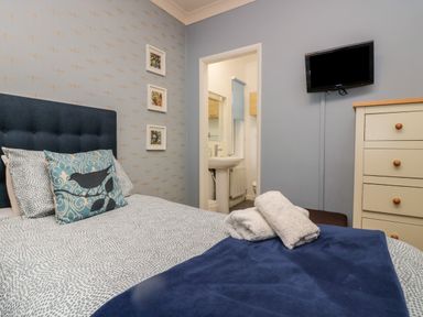 A bedroom with a bed with blue headboard and patterned pillows a chest of drawers and a wall-mounted TV at Sandown in Bowness-on-Windermere