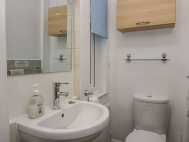 A bathroom with a sink a mirror a toilet a wooden cabinet and a window at Sandown in Bowness-on-Windermere
