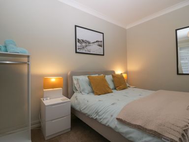 A bedroom with a bed with pillows and blanket bedside tables with lamps a framed picture on the wall and folded towels on a stand at Sandown in Bowness-on-Windermere