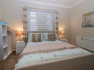 A bedroom with a bed two bedside tables with lamps a window with curtains and an open wardrobe at Sandown in Bowness-on-Windermere