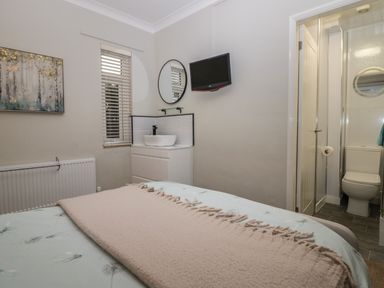 A bedroom with bed blanket wall mounted tv and a sink unit next to a door leading to a bathroom at Sandown in Bowness-on-Windermere