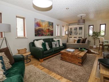 A living room with green and beige sofas a wooden coffee table a white cabinet and a plant at Sandown in Bowness-on-Windermere
