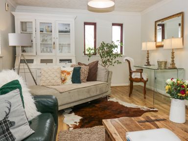 A living room with sofas cushions glass cabinet and flowers on a table at Sandown in Bowness-on-Windermere
