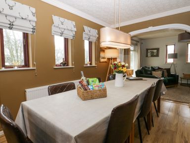 A dining room with a table covered with a cloth surrounded by chairs and a basket with snacks near flowers in a jug at Sandown in Bowness-on-Windermere
