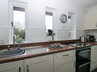 A kitchen with a sink stove kettle utensils and three narrow windows at Sandown in Bowness-on-Windermere