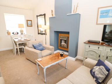 A living room with armchairs a coffee table a fireplace and a dining table in the corner at Driftwood Apartment in Amble-by-the-Sea