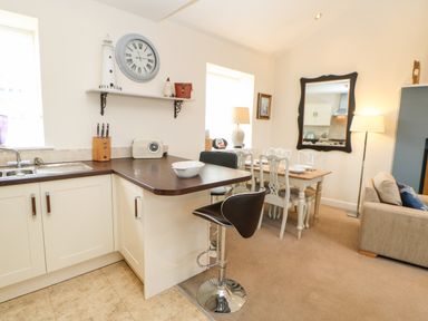 A kitchen with a breakfast bar and stools next to a dining table with chairs and a mirror on the wall at Driftwood Apartment in Amble-by-the-Sea