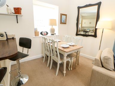 A dining area with a wooden table set for four next to a beige sofa and a bar stool at Driftwood Apartment in Amble-by-the-Sea