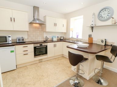 A kitchen with cream cabinets a stainless steel oven and hood a microwave toaster and kettle on the counter at Driftwood Apartment in Amble-by-the-Sea