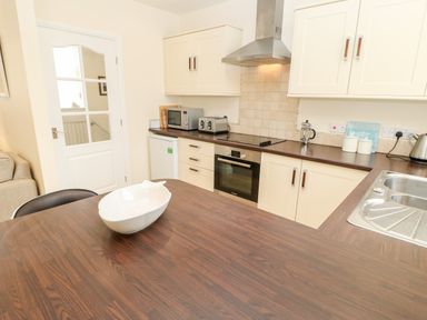 A kitchen with white cabinets dark brown countertops a white bowl on the table a microwave toaster and a stainless steel sink at Driftwood Apartment in Amble-by-the-Sea