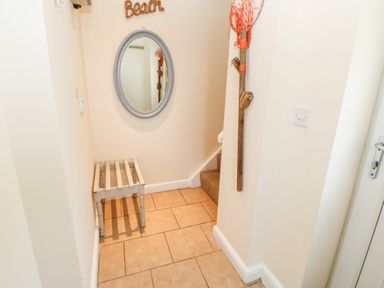 A small hallway with a wooden bench a round mirror and a staircase at Driftwood Apartment in Amble-by-the-Sea