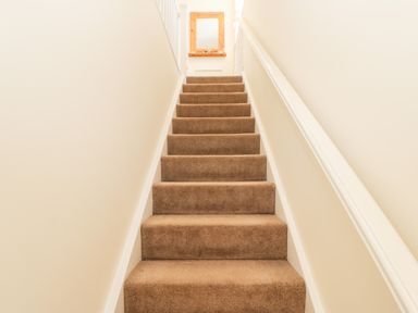 A carpeted staircase with beige walls and a wooden framed mirror at the top at Driftwood Apartment in Amble-by-the-Sea