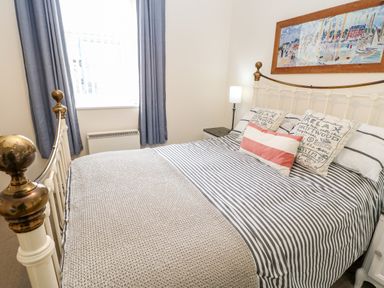 A bedroom with a metal bed frame striped bedding blue curtains and a painting above the bed at Driftwood Apartment in Amble-by-the-Sea