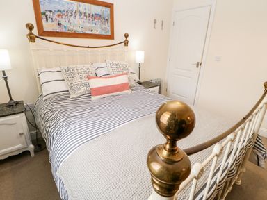 A bedroom with a striped bedspread on a metal bed frame and bedside tables with lamps at Driftwood Apartment in Amble-by-the-Sea