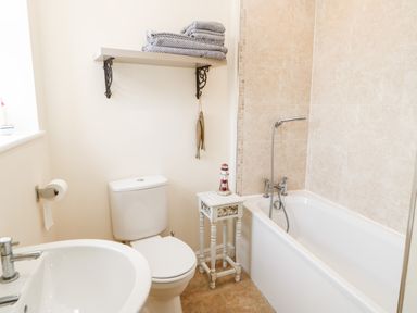A bathroom with a toilet sink bathtub and a small table with a lighthouse decoration at Driftwood Apartment in Amble-by-the-Sea