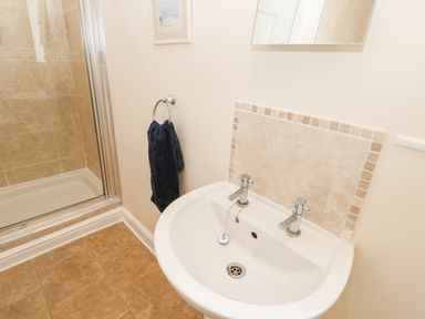 A bathroom sink with two taps and a shower cubicle with tiled walls at Driftwood Apartment in Amble-by-the-Sea