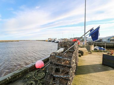 A harbor area with fishing traps on a dock and boats in the water at Driftwood Apartment in Amble-by-the-Sea