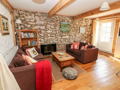 A living room with two brown sofas a wooden coffee table a bookshelf and a stone wall at Beekeeper's Cottage in Pembroke