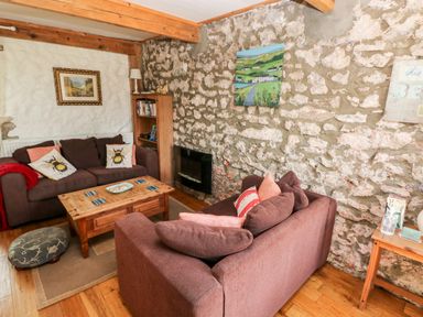 A living room with two brown sofas a wooden coffee table and stone walls at Beekeeper's Cottage in Pembroke
