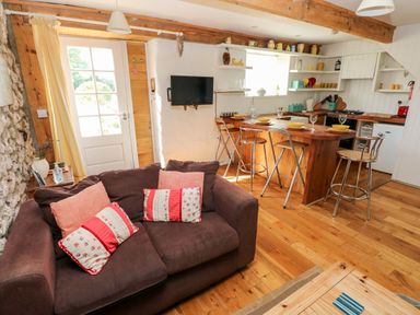 A living room with a sofa and cushions next to a kitchen with a wooden island and bar stools at Beekeeper's Cottage in Pembroke