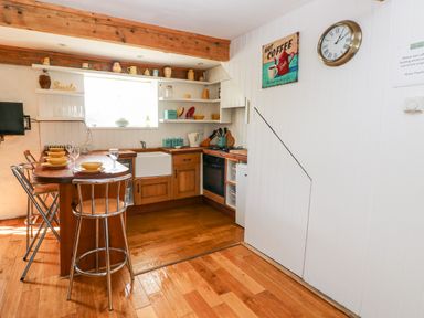 A kitchen with wooden cabinets a breakfast bar with stools a farmhouse sink and open shelves at Beekeeper's Cottage in Pembroke
