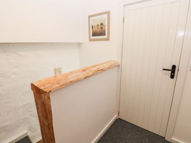 A hallway with a wooden handrail on a white half wall next to a white paneled door with a black handle at Beekeeper's Cottage in Pembroke