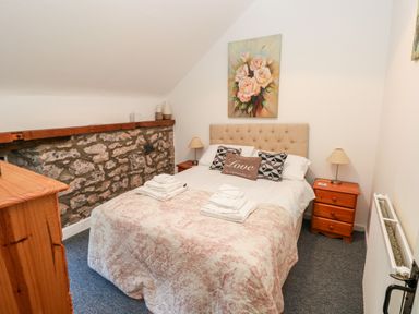 A bedroom with a double bed bedside tables lamps and a stone wall at Beekeeper's Cottage in Pembroke