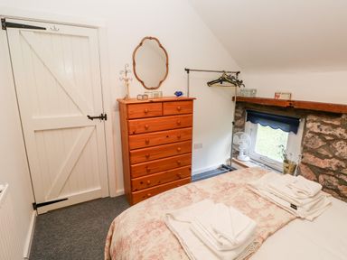 A bedroom with a wooden chest of drawers a mirror a bed with folded towels and a small window with a fan at Beekeeper's Cottage Pembroke