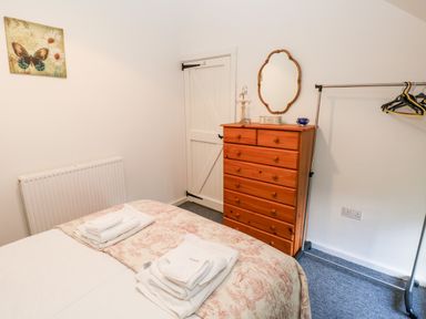 A bedroom with a bed with folded towels a wooden chest of drawers a mirror a door and a clothes rack at Beekeeper's Cottage in Pembroke