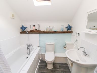 A bathroom with a bathtub shower combination toilet sink and a wooden shelf with decorative items at Beekeeper's Cottage in Pembroke