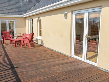 A wooden deck with red patio furniture and glass doors at Bluebell House and Gardens in Gurteenulla near Ballydehob County Cork