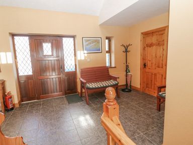 A hallway with a wooden front door a wooden bench a coat rack an umbrella and a fire extinguisher at Bluebell House and Gardens Gurteenulla near Ballydehob County Cork