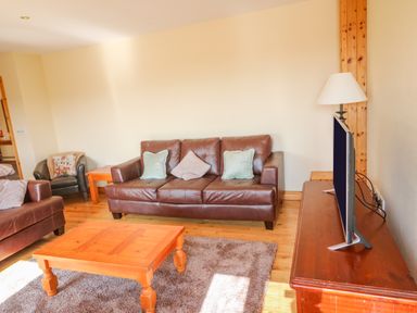 A living room with brown leather sofas wooden coffee table and a television on a wooden cabinet at Bluebell House and Gardens in Gurteenulla near Ballydehob County Cork