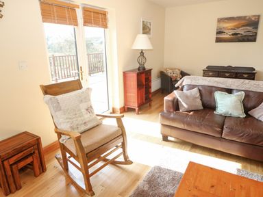 A living room with brown leather sofa wooden rocking chair small wooden tables and glass door at Bluebell House and Gardens in Gurteenulla near Ballydehob County Cork